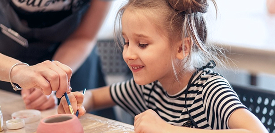 Девочка раскрашивает глиняное изделие.